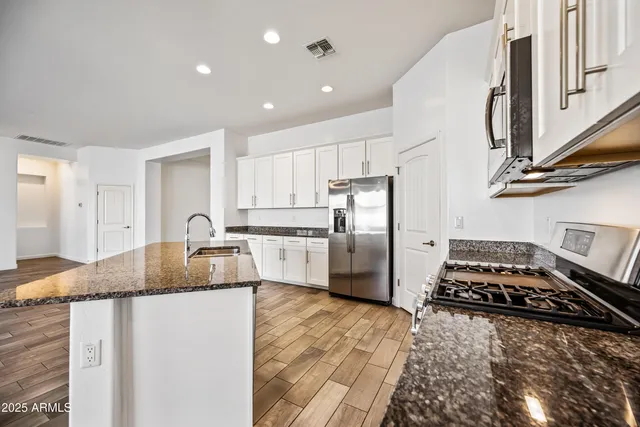 a kitchen with granite countertop a refrigerator a sink a stove and white cabinets