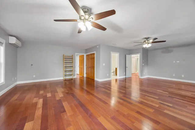 a view of an empty room with wooden floor and a ceiling fan