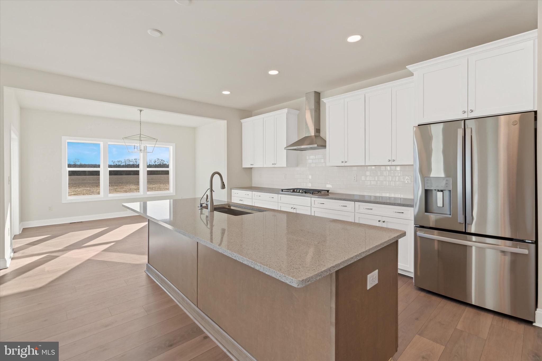 22484 Hummingbird Road, Unit 13 Ellendale, DE 19941 - Photo 10 of 34 a large kitchen with kitchen island a stove a refrigerator a sink and white cabinets with wooden floor
