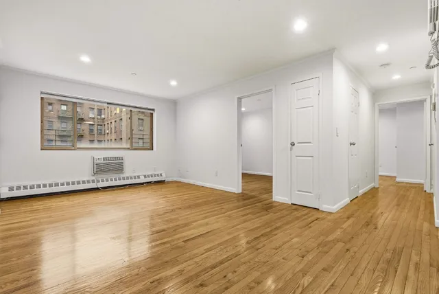 a view of empty room with wooden floor and kitchen view