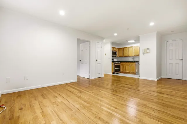 an empty room with wooden floor and kitchen view