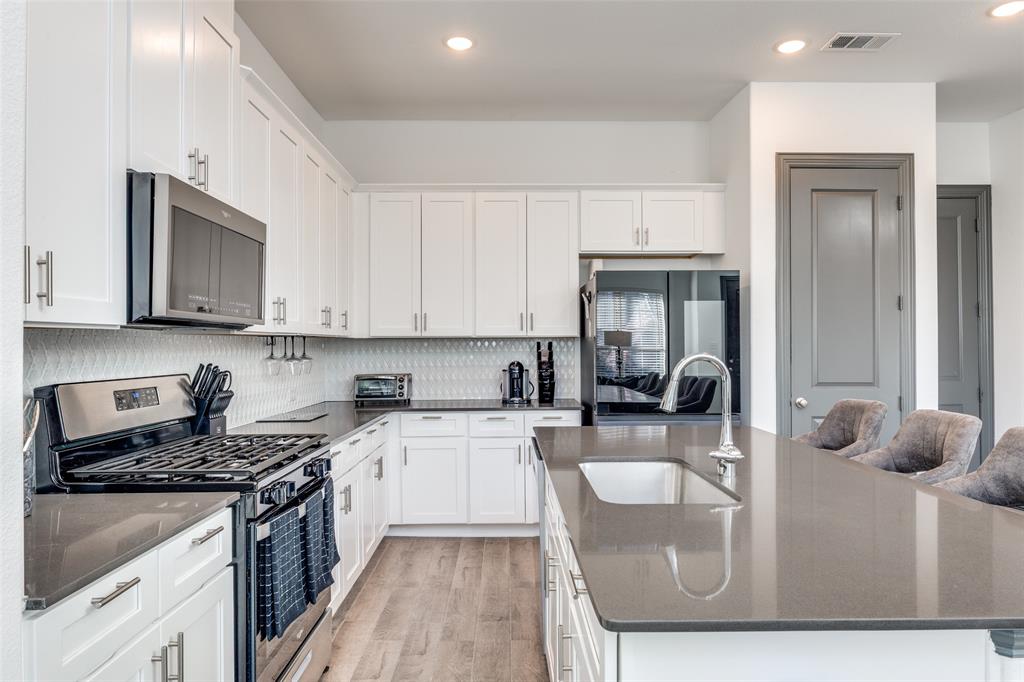 8132 Foraker Street Frisco, TX 75034 - Photo 8 of 25 Kitchen with dark stone countertops, stainless steel appliances, a center island with sink, white cabinetry, and recessed lighting