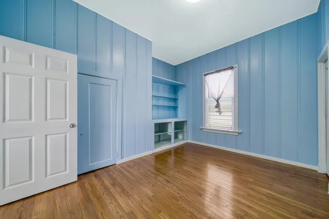 an empty room with wooden floor cabinet and windows