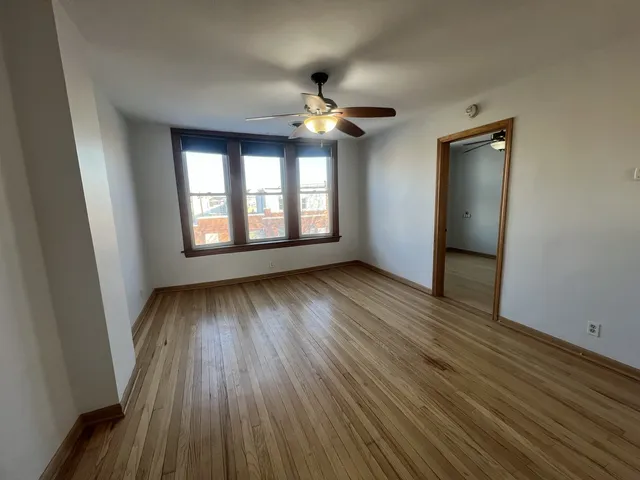 an empty room with wooden floor chandelier fan and windows