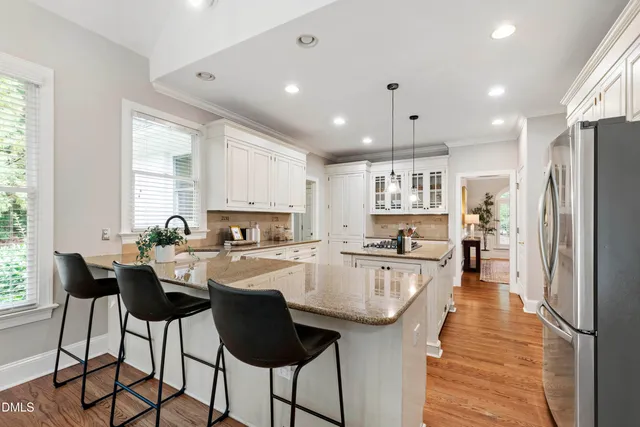 a kitchen with stainless steel appliances granite countertop a refrigerator a sink dishwasher a dining table and chairs with wooden floor