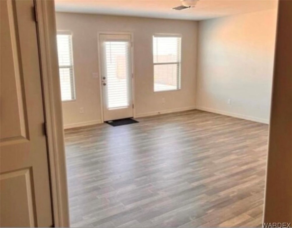 3665 East Koval Road Kingman, AZ 86409 - Photo 8 of 10 Spacious room featuring wood-look flooring, neutral wall tones, and a glass-paned door with blinds, providing access to the outside