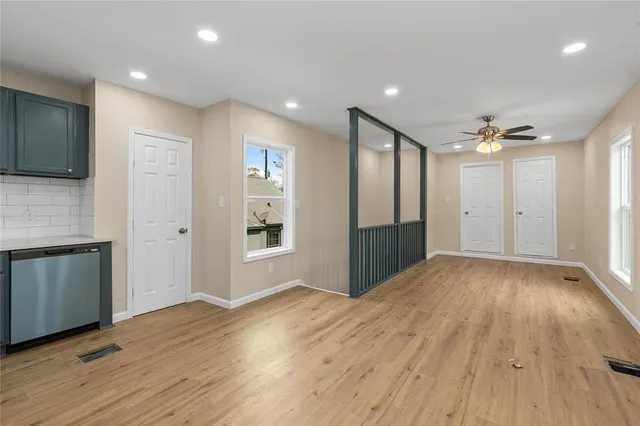 a view of an empty room with wooden floor and a kitchen