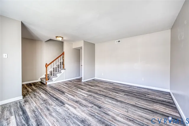 a view of an empty room with wooden floor and stairs