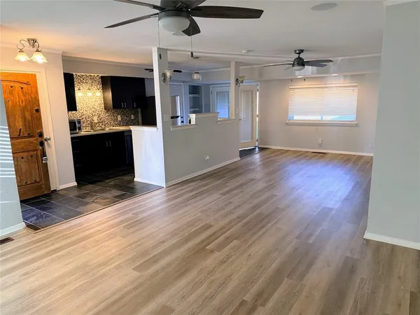 an empty room with wooden floor kitchen view and a window