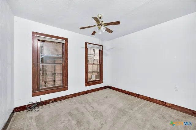 an empty room with chandelier fan and windows