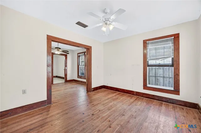 an empty room with wooden floor chandelier and windows
