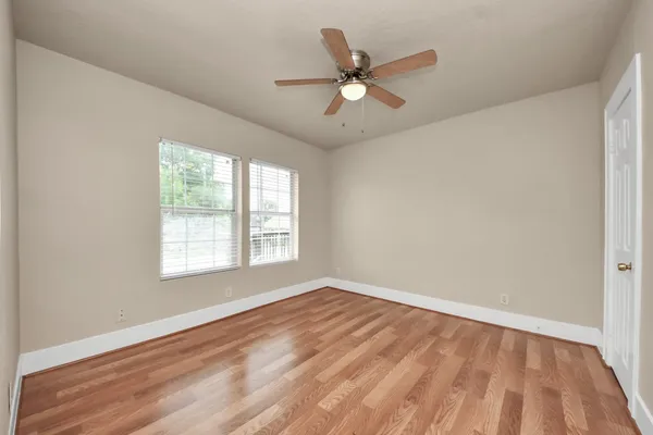 an empty room with wooden floor fan and windows