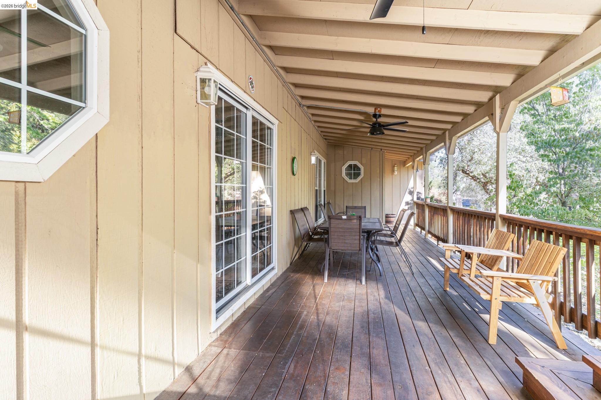 Expansive covered wood-finish deck with a ceiling fan, wood railing, and multiple sliding glass door entries
