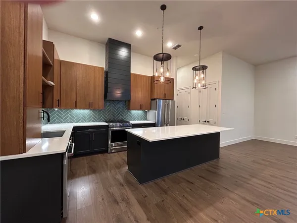 a large kitchen with stainless steel appliances a large counter top a stove a sink and a wooden floors