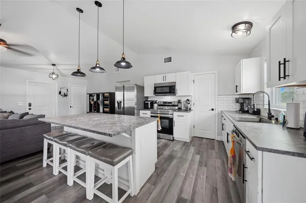 a large kitchen with stainless steel appliances granite countertop a stove oven a sink dishwasher and a refrigerator with wooden floor