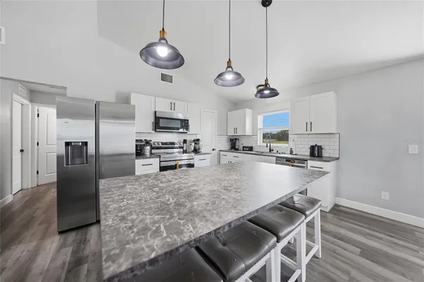 a kitchen with stainless steel appliances granite countertop a sink a stove a refrigerator cabinets and chairs