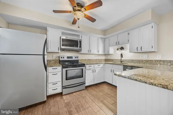 a kitchen with granite countertop a refrigerator a sink dishwasher a stove and white cabinets with wooden floor