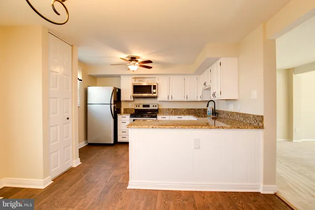 a kitchen with stainless steel appliances granite countertop a refrigerator a stove a sink and white cabinets with wooden floor