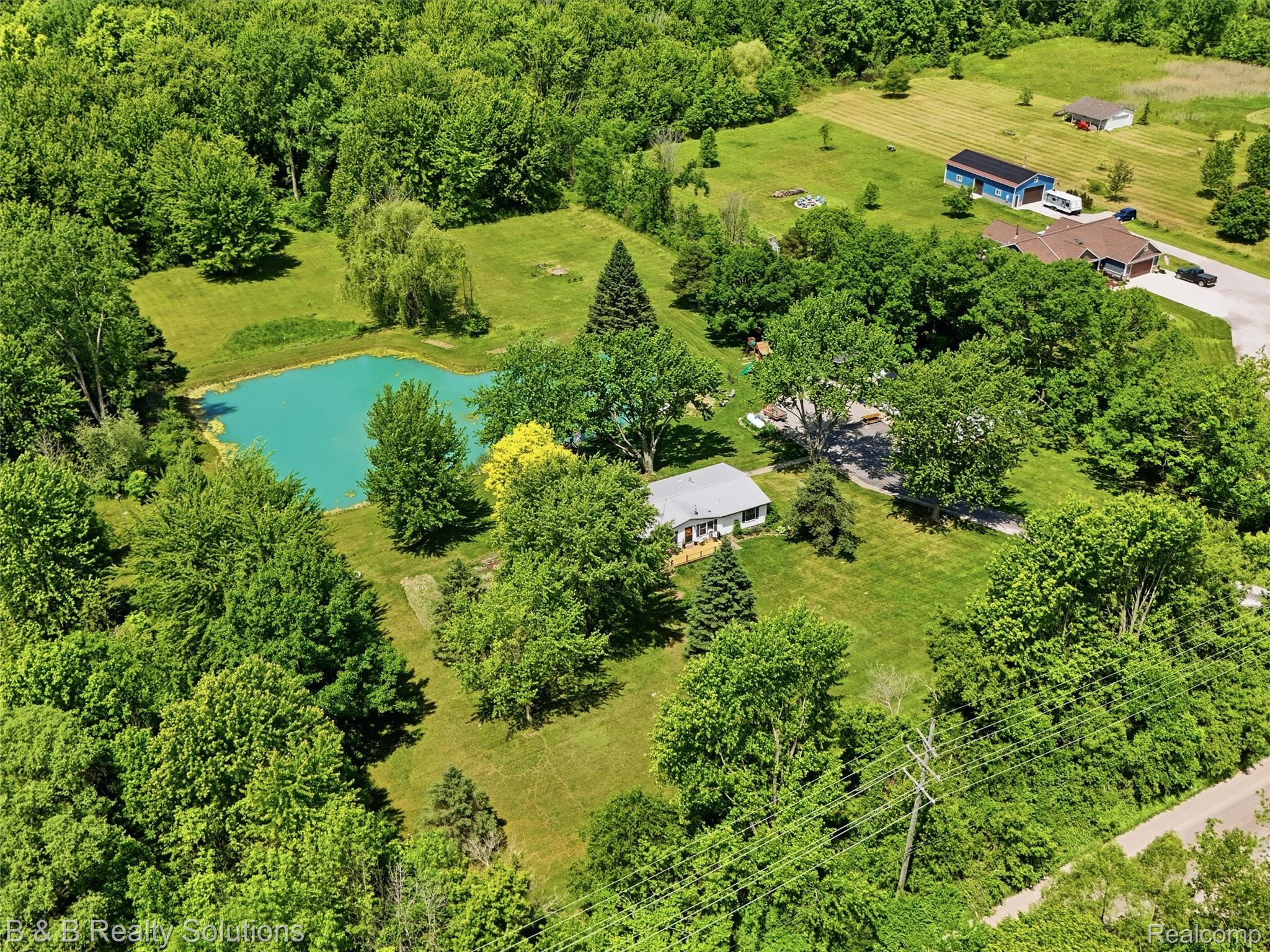 60455 Bates Road New Haven, MI 48048 - Photo 14 of 58 Spacious property featuring a bright blue pond, extensive green lawn, and mature trees