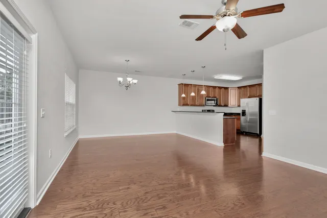 an empty room with wooden floor a kitchen view and a window