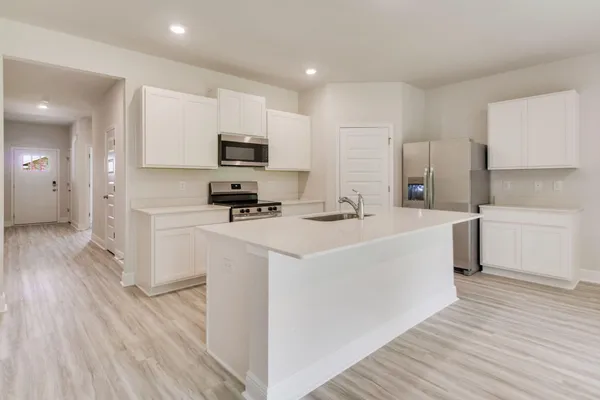 a kitchen with stainless steel appliances a microwave a stove a sink and white cabinets with wooden floor