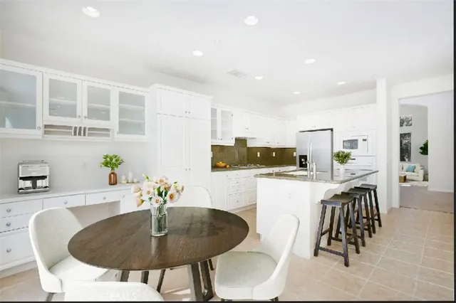 a kitchen with stainless steel appliances kitchen island granite countertop a dining table chairs and a refrigerator