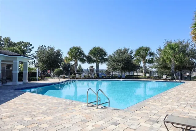 a view of swimming pool with seating space and trees in the background