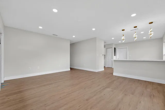 a view of an empty room with wooden floor and kitchen