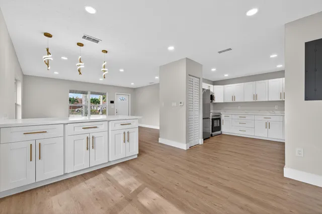 a large kitchen with stainless steel appliances kitchen island a sink dishwasher a refrigerator and white cabinets with wooden floor