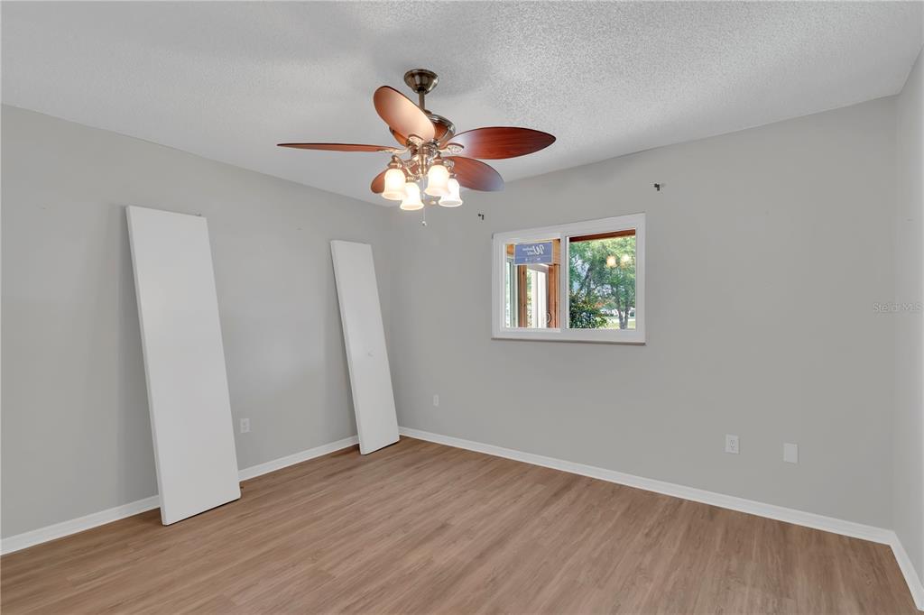 6366 Southwest 115th Street Road Ocala, FL 34476 - Photo 21 of 45 an empty room with wooden floor chandelier fan and windows