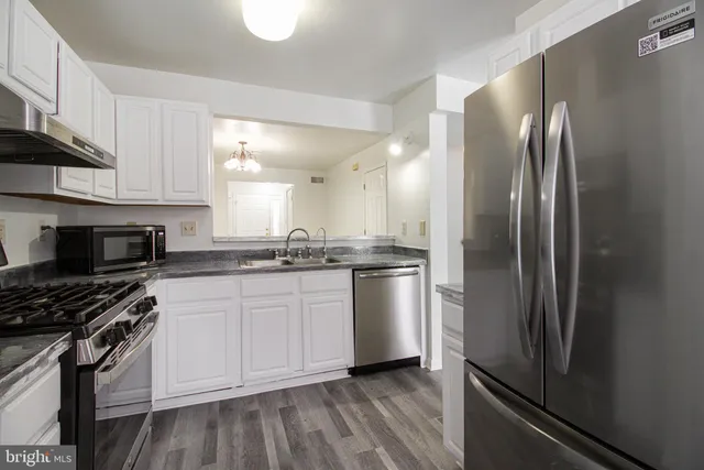 a kitchen with stainless steel appliances granite countertop a refrigerator a stove and a sink with wooden floor