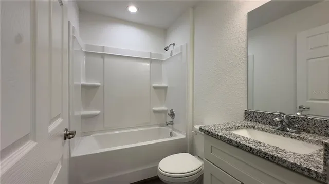 a bathroom with a granite countertop bathtub shower sink vanity and toilet