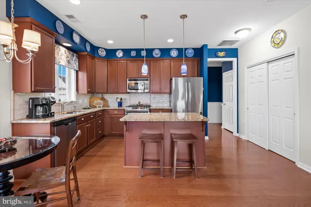 a kitchen with stainless steel appliances granite countertop a refrigerator a sink dishwasher a stove and a dining table with wooden floor