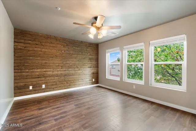 an empty room with wooden floor chandelier fan and windows