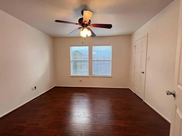 an empty room with wooden floor fan and windows
