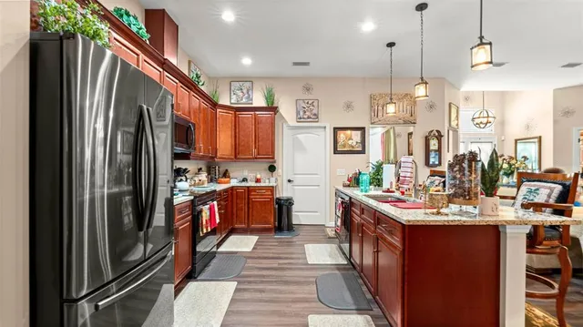 a kitchen with stainless steel appliances granite countertop a refrigerator a sink dishwasher a stove and a dining table with wooden floor