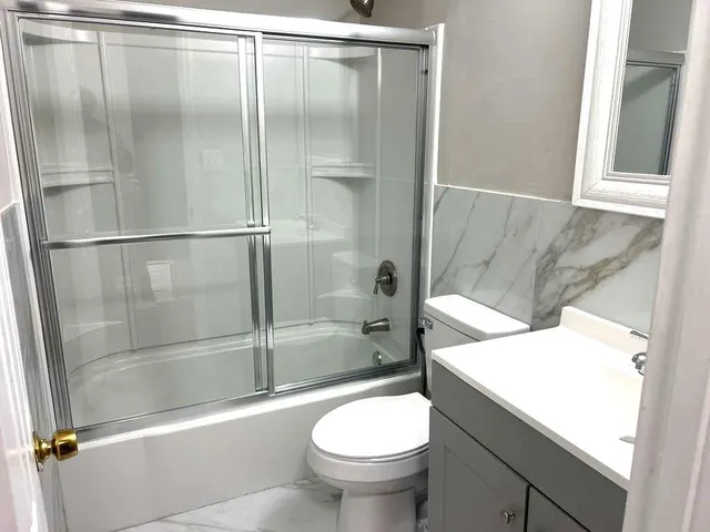 a bathroom with a granite countertop bathtub shower sink mirror and toilet