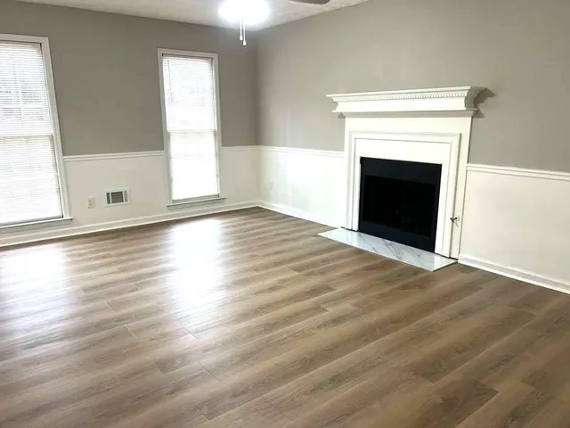an empty room with wooden floor fireplace and windows