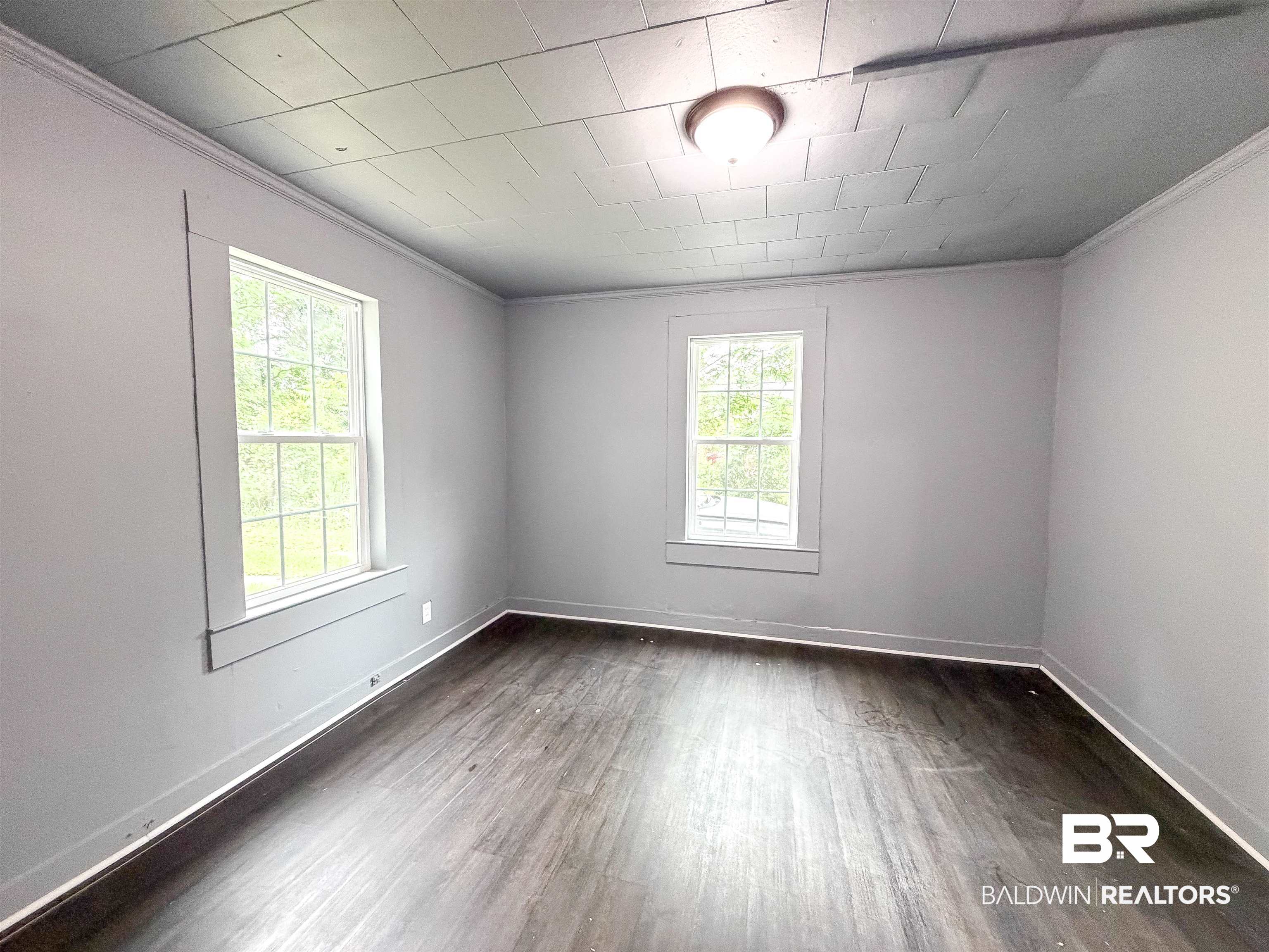 38 Flock Avenue Mobile, AL 36610 - Photo 12 of 27 Interior space featuring two windows with white trim, dark wood-finish flooring, light gray walls, and a recessed ceiling light fixture