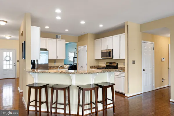 a kitchen with stainless steel appliances kitchen island granite countertop a stove a sink dishwasher and a microwave oven with white cabinets
