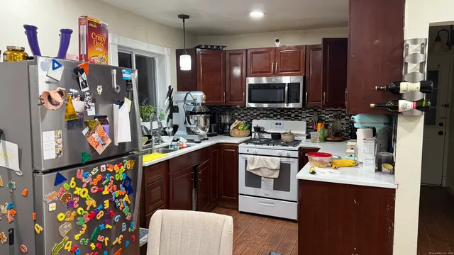 a kitchen with stainless steel appliances kitchen island granite countertop a sink dishwasher and a refrigerator with wooden floor