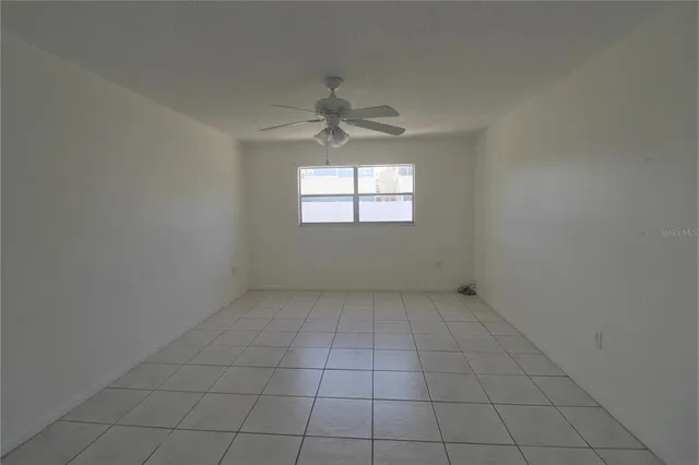 an empty room with a chandelier fan and windows