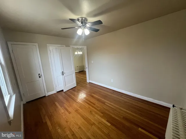 a view of an empty room with wooden floor and fan