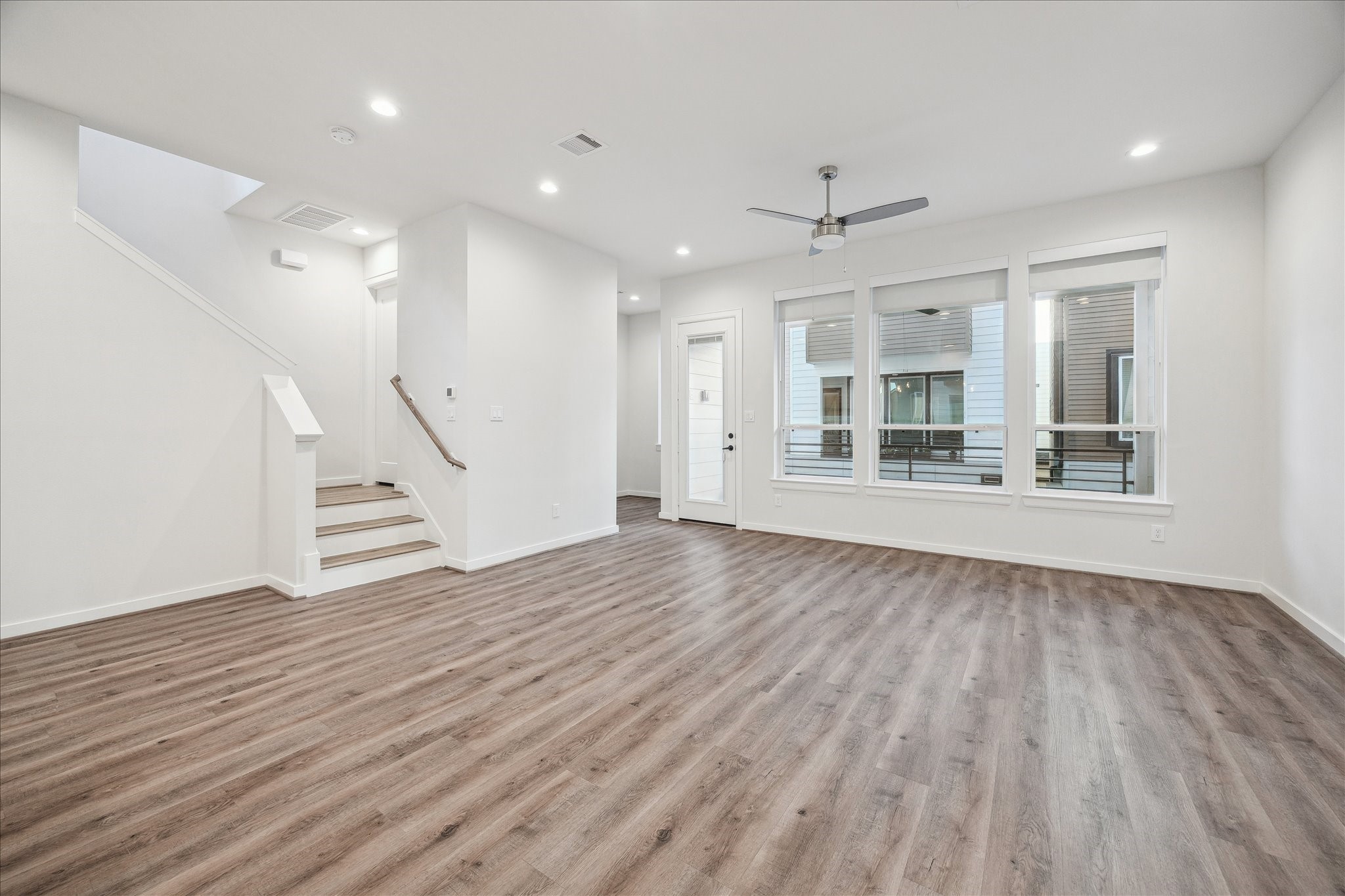 1603 Patterson Street, Unit E Houston, TX 77007 - Photo 16 of 32 This spacious, modern living area features sleek wood flooring, large windows offering ample natural light, a ceiling fan, and an open layout with white walls. A staircase leads to the upper floor, enhancing the room's airy feel.