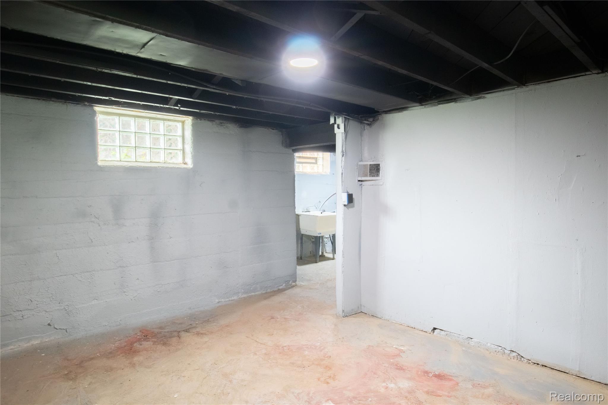 633 Perry Street Pontiac, MI 48342 - Photo 22 of 26 Finished basement area featuring painted concrete walls, exposed ceiling joists, and a glass block window