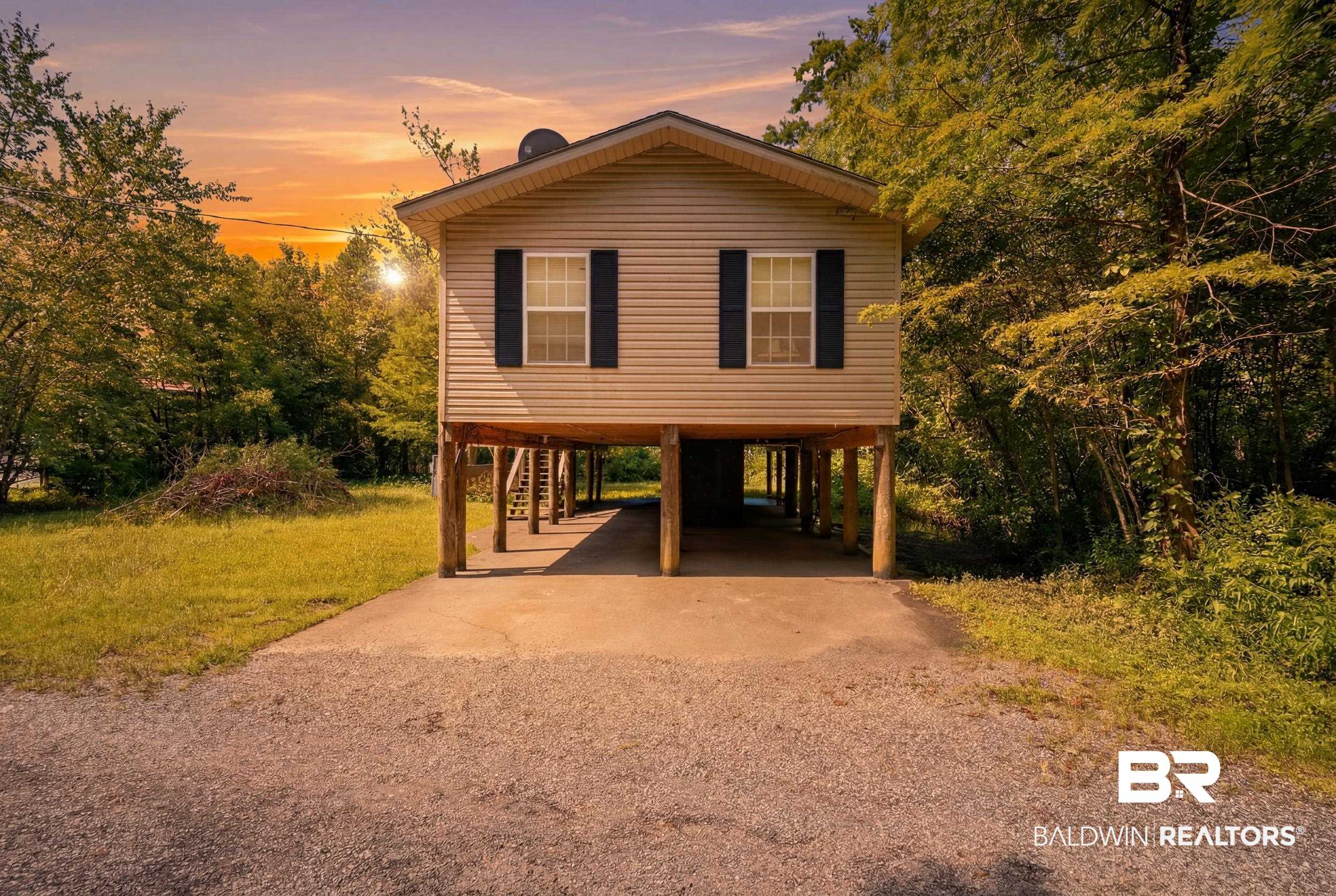 42080 Bayou Road Bay Minette, AL 36507 - Photo 1 of 43 Elevated beige siding home featuring black louvered shutters, a covered parking area, and a surrounding wooded landscape