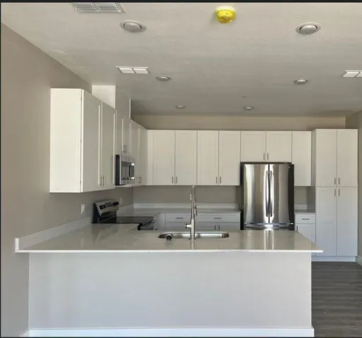 a kitchen with stainless steel appliances a sink a stove a microwave a refrigerator and white cabinets