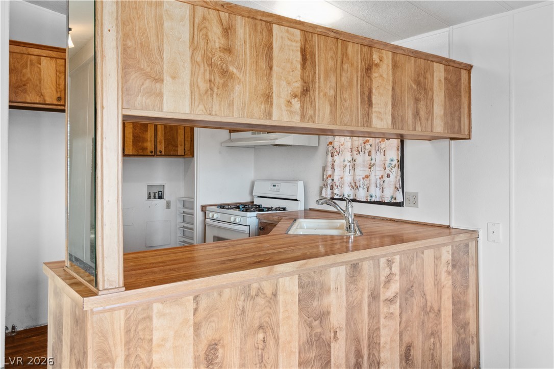 1671 Granada Street Laughlin, NV 89029 - Photo 11 of 63 Kitchen with under cabinet range hood, white gas range, brown cabinetry, and a sink