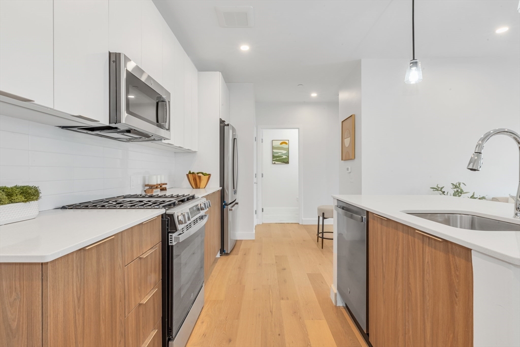 3992 Washington Street, Unit 302 Boston, MA 02131 - Photo 13 of 29 a large kitchen with stainless steel appliances granite countertop a sink and stove top oven with wooden floor