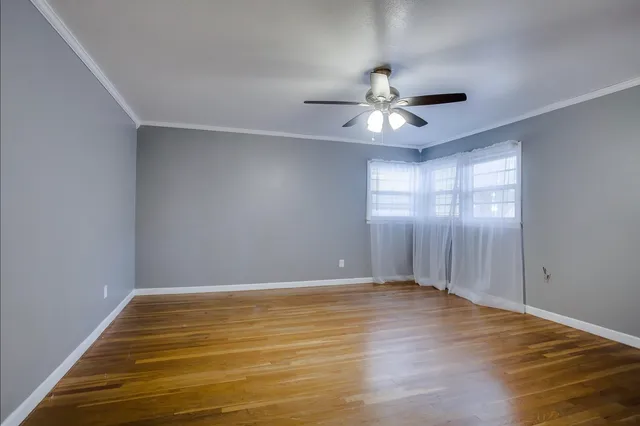 an empty room with wooden floor chandelier fan and windows